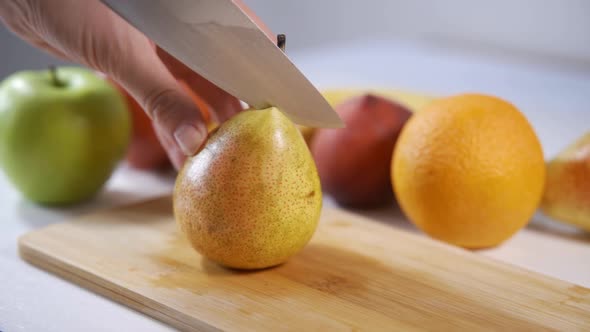 Graceful Female Hands Cut a Large Pear in Half with a Large Knife
