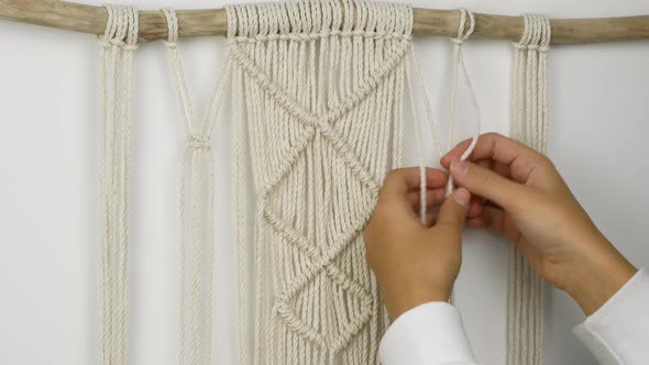 A woman weaves with her own hands a pattern of Macrame threads for decoration or home decor.