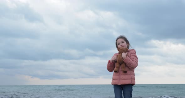 Little Girl Hugs a Teddy Bear on the Beach