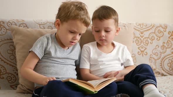 Two Little Boys Are Reading Book Sitting on a Sofa