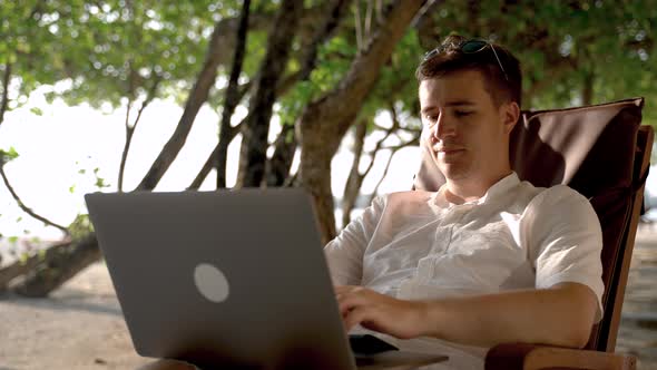 The Pensive Businessman Looks Towards the Beach and Continues to Work at Laptop alt