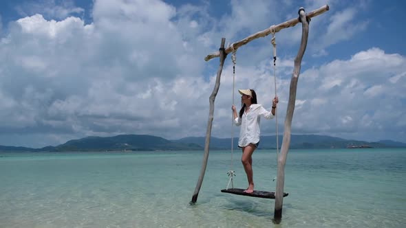 Slow motion of a beautiful young asian woman standing on wooden swing in the sea