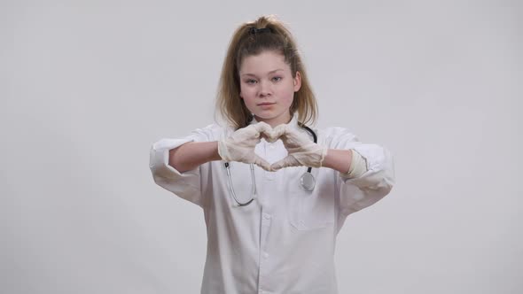 Caucasian Girl in Medical Uniform Showing Heart Shape with Hands Smiling Looking at Camera alt