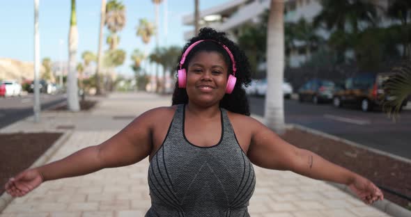 Curvy latin woman smiling in camera while doing jogging routine outdoor in the city alt