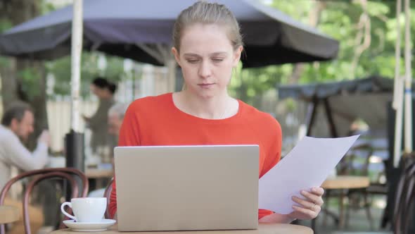 Young Woman Reading Contract and Using Laptop Sitting in Cafe Terrace alt