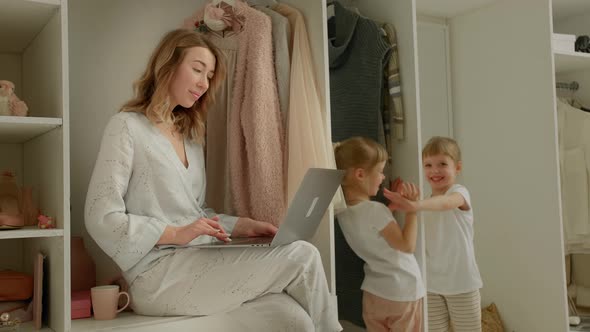 Girl with a Laptop Sits on the Closet and Looks at the Playing Children
