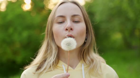 A Beautiful Young Woman Stands in the Forest and Blows a Dandelion, On the Street, Enjoy Nature alt