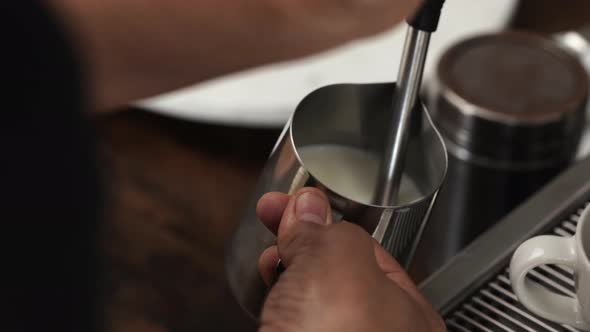 Barista making milk foam in stainless steel pitcher with coffee maker steam wand