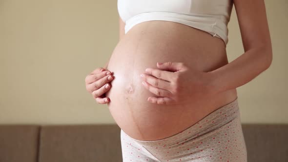 Beautiful Pregnant Woman and Her Handsome Husband Hugging the Tummy While in Light Room alt