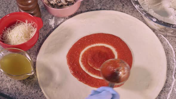 The pizza maker adds red sauce to the base of the pizza