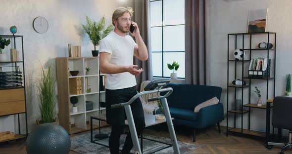 Guy in Sportswear Talking on Phone while Walking on Running Track During Home Workout alt