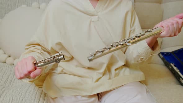 A woman hand with a flute is playing at home on the sofa in the living room, close-up alt