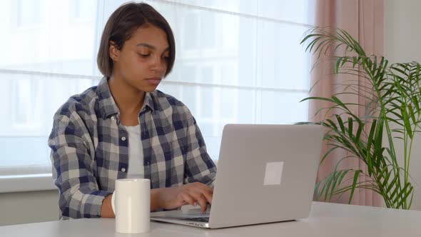 A Young Woman Using a Laptop is Studying Online at Home