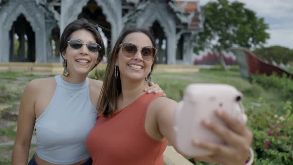 Two Happy Women Tourists Taking Selfies Using An Instant Print Camera With Beautiful Pavillion And alt
