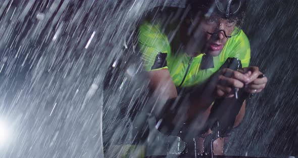 Triathlon Athlete Riding a Professional Racing Bicycle on an Intense Workout in Dark with Rain alt