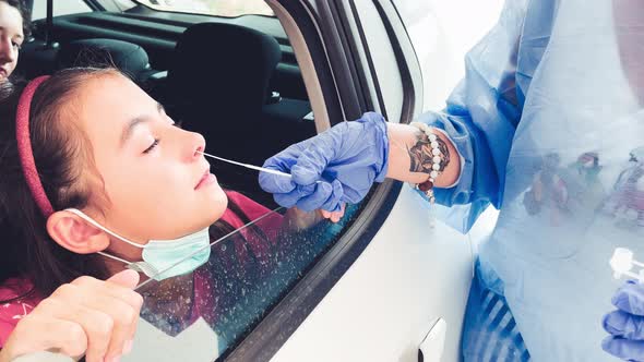 Doctor Taking a Swab for Nasal Test Sample Fom Elementary Age Girl's Lips Performing Covidtest alt