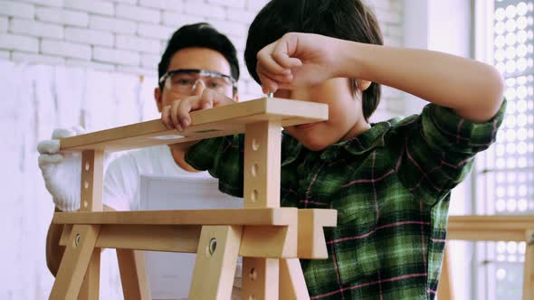 Young male carpenter teaching his son how to work with wood in workshop. alt