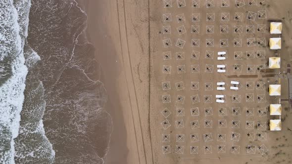 aerial empty beach with straw sunshades and sunbeds near sea waves