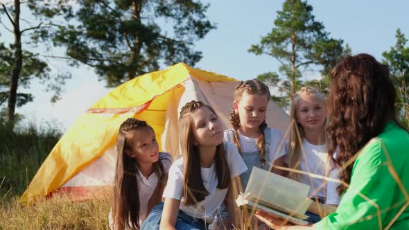 A Young Teacher Reads a Book to Girls in a Summer Camp Through the Work of an Educator alt