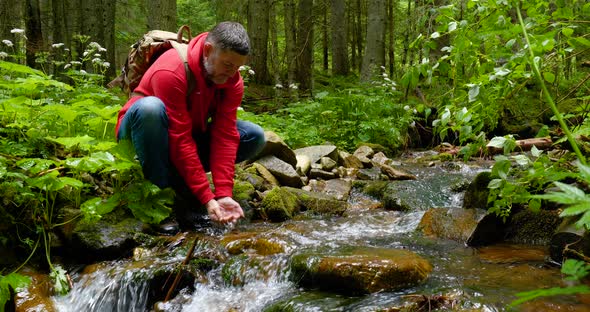 A Bearded Man with a Backpack Drinks Water From a Mountain Stream alt