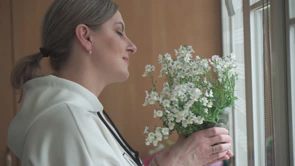 A Young Woman Looks at Flowers She Has Grown at Home