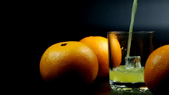 Orange Juice And A Few Oranges Are Poured Into A Glass On A Black Background