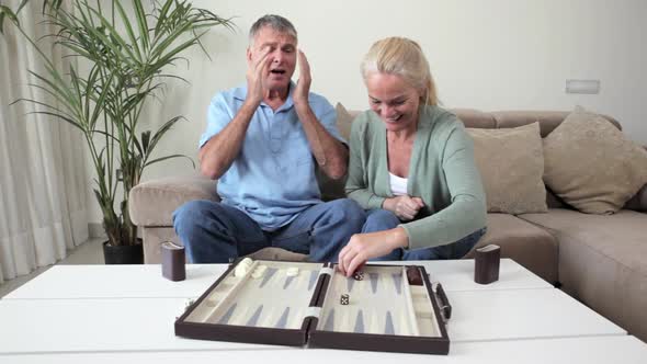 Mature couple playing backgammon, woman making winning move alt