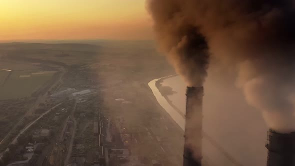 Aerial view of coal power plant high pipes with black smoke moving up polluting atmosphere at sunset alt
