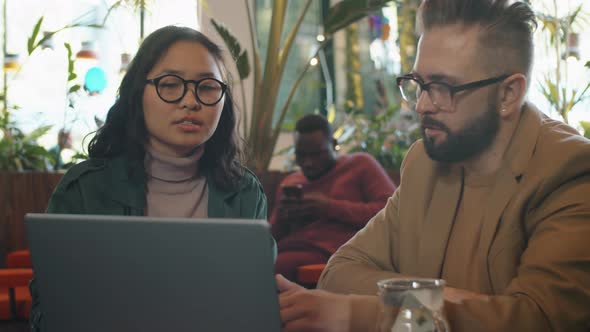 Multiethnic Business Partners Drinking Tea and Using Laptop in Cafe alt