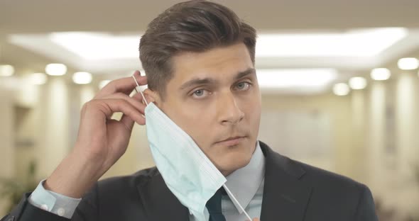 Close-up of Brunette Businessman Putting on Face Mask in Office. Portrait of Serious Handsome Tanned alt