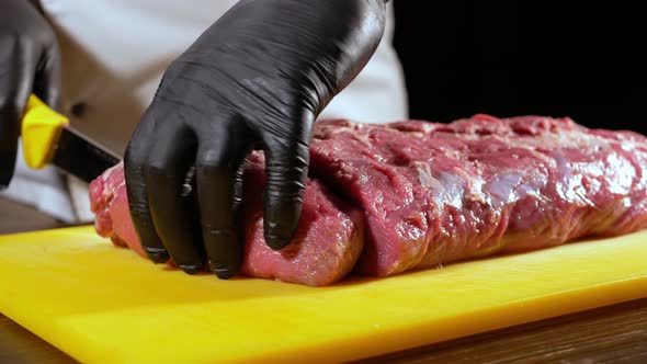 A Professional Butcher in Black Gloves Slices a Piece of Raw Meat for Steak From Entrecote with a