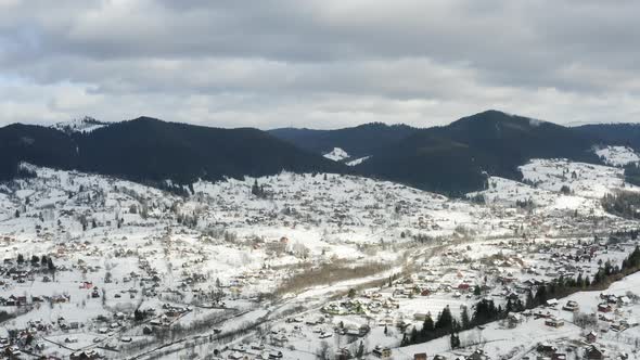 Aerial view of a Mountain Village with Hills Covered in Snow and Pine Forest in Winter