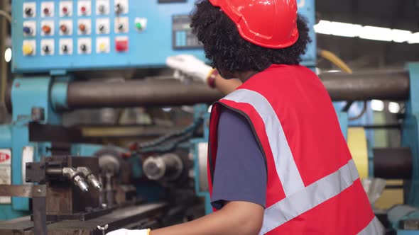African American female worker in safety uniform checking on factory machine