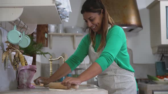 Mature Latin woman kneading flour dough with rolling pin in old vintage kitchen alt
