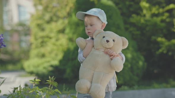 Lost Baby Boy Child in Cap Walking Street with Backpack and Teddy Bear in Hands alt