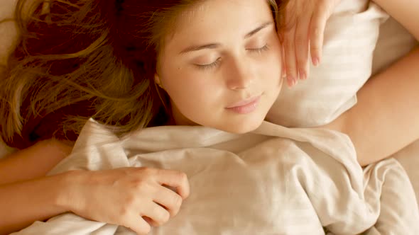Calm young woman lying in bed and sleeping on pillow, girl resting, enjoying sunny morning, top view