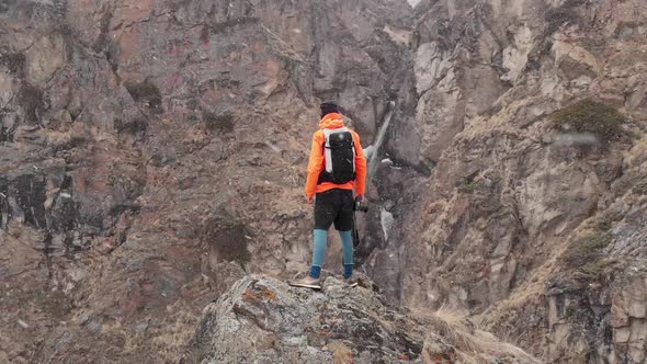 Aerial View of a Young Male Photographer with a Camera in His Hands Stands on a High Rock in a Gorge alt