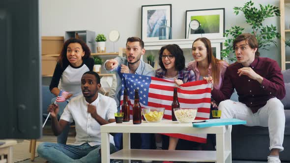American Fans Watching Sports on TV at Home Hugging Laughing and Doing High-five alt