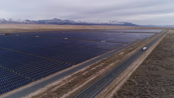 Trucks on the highway next to solar farm looking towards snow capped mountains alt