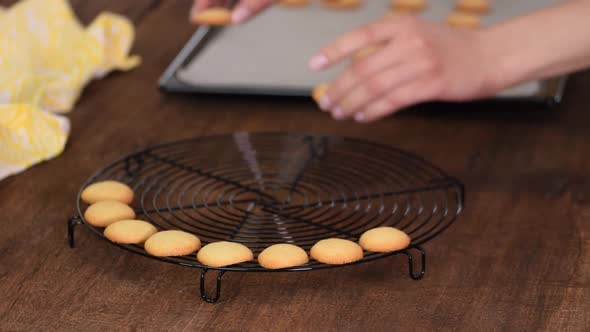 Pastry chef woman putting small vanilla cookies on a cooling rack.