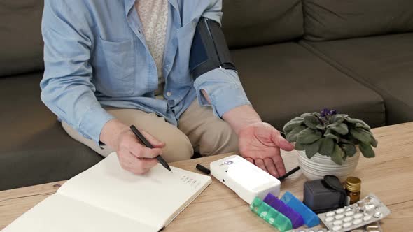 An Elderly Woman Measures Her Blood Pressure and Writes Down the Results in a Notebook