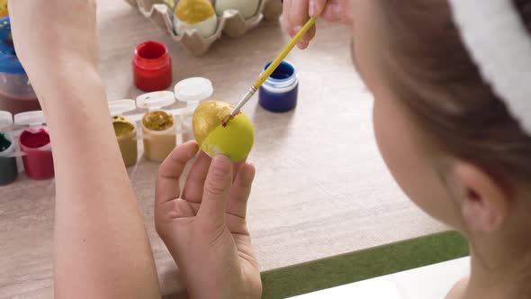 Top View of a Girl Decorating an Easter Egg in Yellow with a Red Stripe