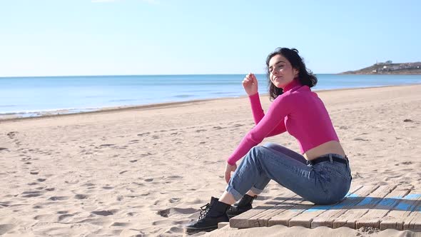 Young Woman Sitting on the Sand Beach and Smiling and Fixing Her Hair