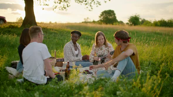 Young Multiethnic Friends Have Fun at a Picnic Play Ukulele or Guitar Sing