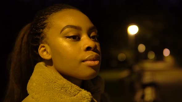 A Young Black Woman Looks Around in a City Park at Night  Face Closeup alt