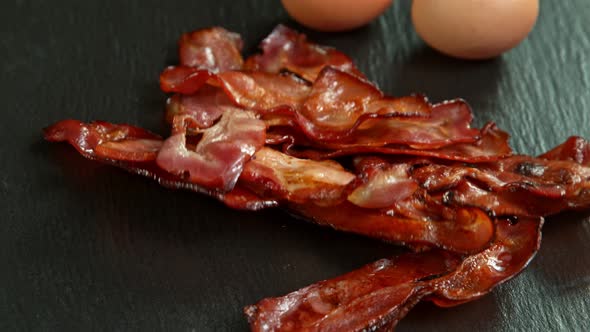 Super Slow Motion Shot of Roasted Bacon Slices Falling on Black Table at 1000 Fps alt