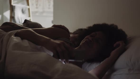 Mixed Race Couple waking up in bed looking at alarm on smart phone