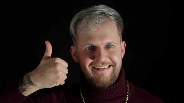 Smiling Man in Stylish Blouse Looking Approvingly at Camera Showing Thumbs Up on Black Background alt