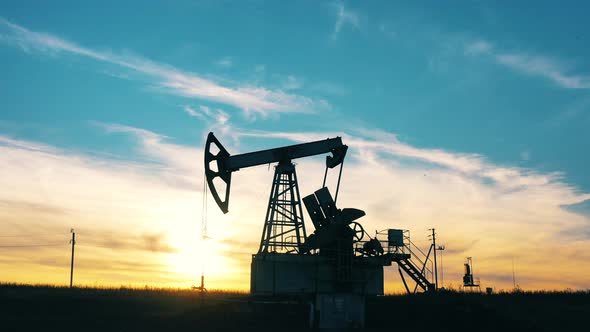 Silhouette of a Working Oil Pumpjack in an Oil Field at Sunset alt