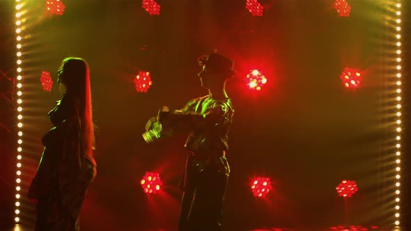 Silhouette Couple Dancers in Romany Clothes Dancing Merrily in Dark Studio Against Background of alt